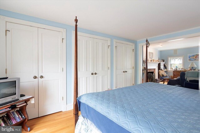 bedroom featuring light wood-type flooring, a fireplace, and multiple closets