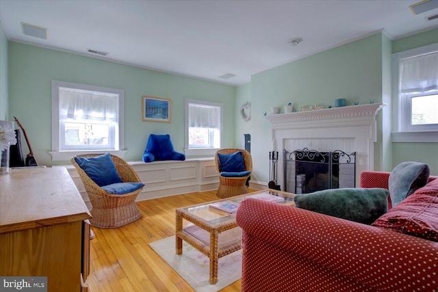 living room featuring crown molding, light wood finished floors, visible vents, and a fireplace