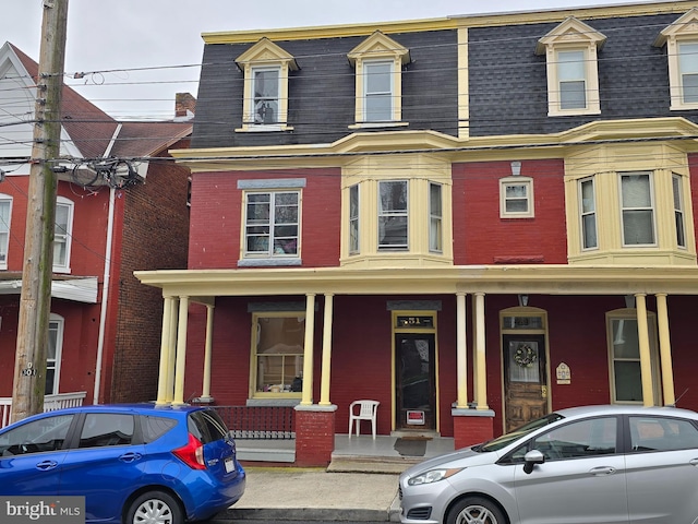 view of front of house with brick siding, a porch, a shingled roof, and mansard roof