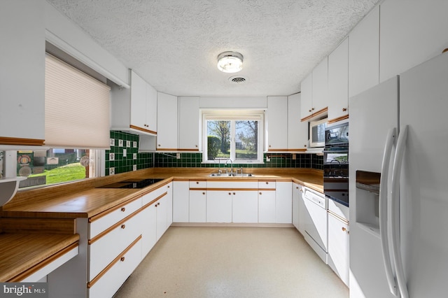 kitchen with backsplash, visible vents, a sink, black appliances, and white cabinetry