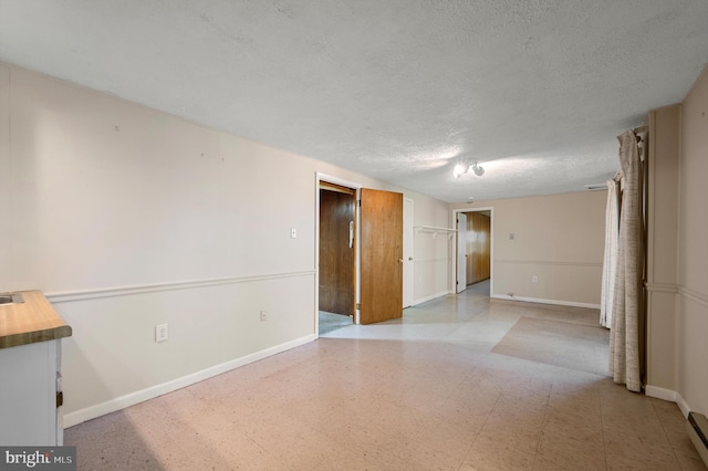 spare room featuring a baseboard radiator, a textured ceiling, baseboards, and light floors