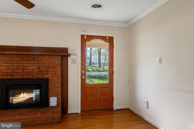 doorway featuring wood finished floors, visible vents, crown molding, baseboards, and a brick fireplace