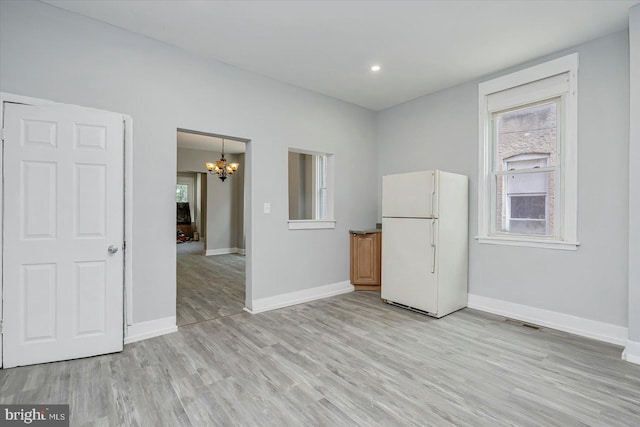 empty room featuring a chandelier, light wood finished floors, and baseboards