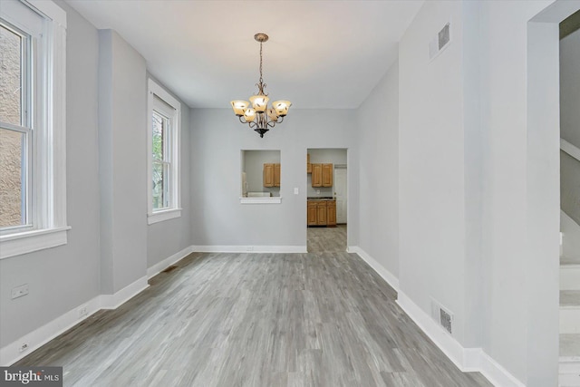 unfurnished dining area featuring a chandelier, light wood finished floors, and baseboards