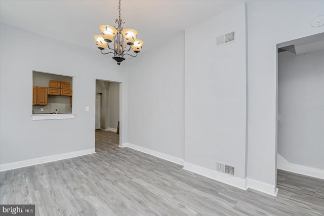 unfurnished living room with a chandelier, light wood finished floors, and baseboards
