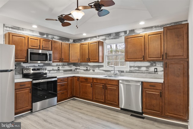 kitchen with a ceiling fan, appliances with stainless steel finishes, light countertops, a sink, and a raised ceiling