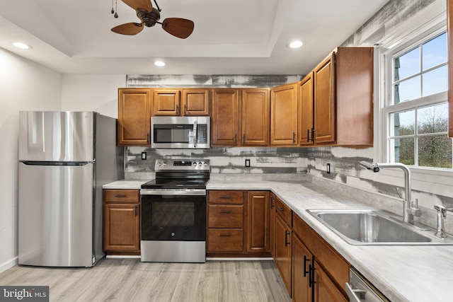 kitchen with a raised ceiling, a sink, appliances with stainless steel finishes, a ceiling fan, and decorative backsplash