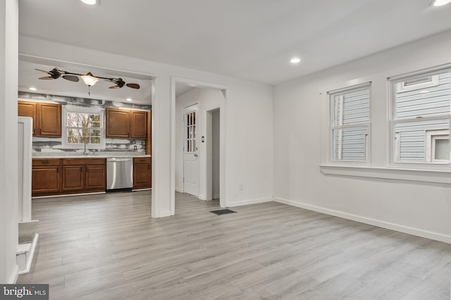 kitchen with baseboards, light countertops, light wood-type flooring, brown cabinetry, and stainless steel dishwasher