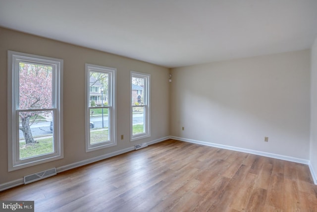 spare room with light wood-style floors, a healthy amount of sunlight, baseboards, and visible vents