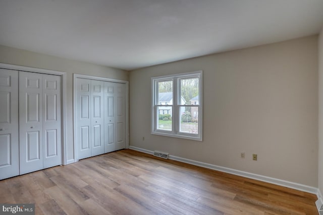 unfurnished bedroom featuring multiple closets, baseboards, light wood-type flooring, and visible vents