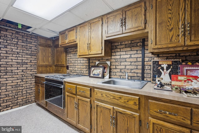 kitchen with brick wall, light countertops, gas stove, and a sink