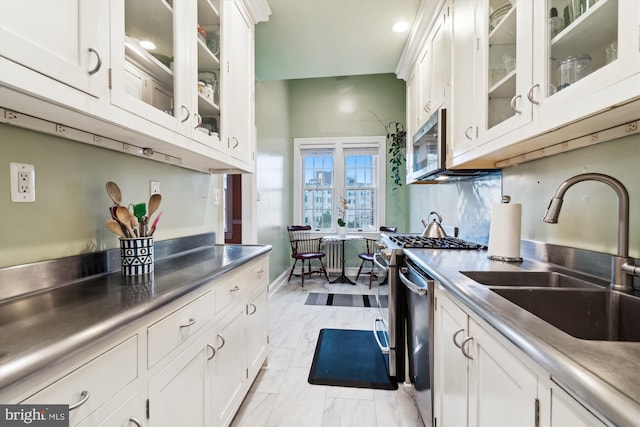 kitchen with a sink, appliances with stainless steel finishes, white cabinetry, stainless steel counters, and marble finish floor