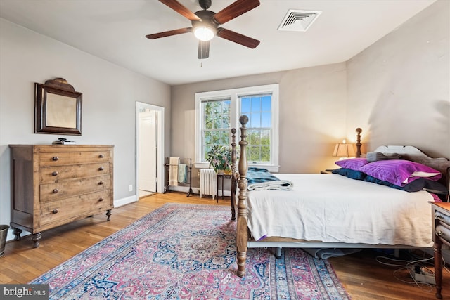 bedroom featuring radiator, a ceiling fan, visible vents, wood finished floors, and baseboards