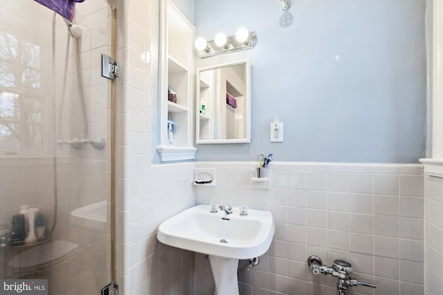 bathroom featuring a sink, tile walls, a stall shower, and a wainscoted wall