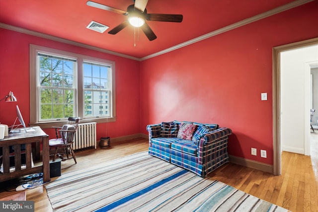 living area with radiator heating unit, ornamental molding, visible vents, hardwood / wood-style floors, and baseboards