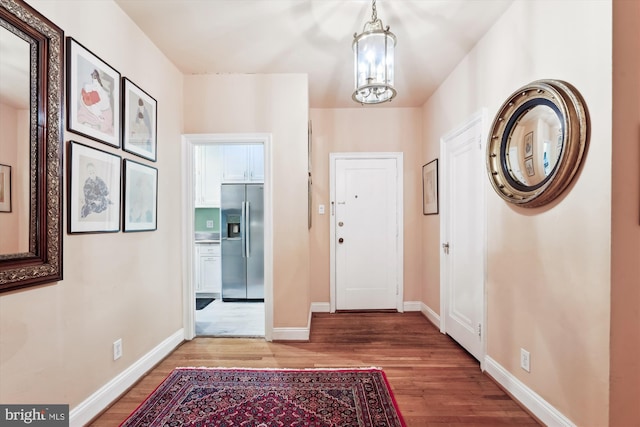 foyer entrance featuring wood finished floors, a notable chandelier, and baseboards