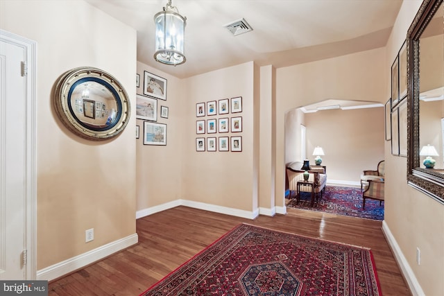 corridor featuring baseboards, an inviting chandelier, visible vents, arched walkways, and wood finished floors