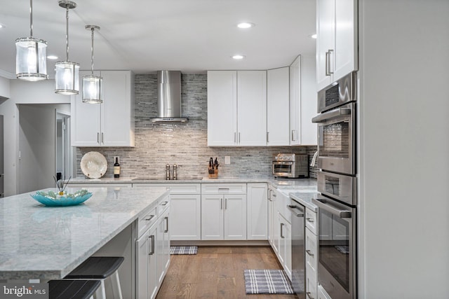 kitchen featuring decorative backsplash, wall chimney exhaust hood, white cabinets, and double oven