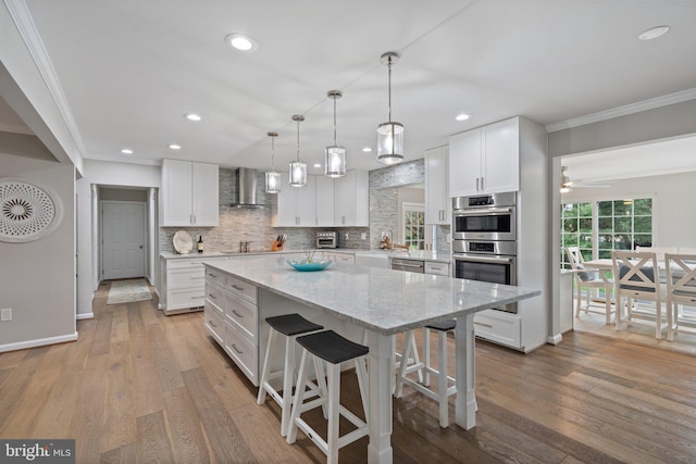 kitchen with crown molding, appliances with stainless steel finishes, wall chimney range hood, and a center island