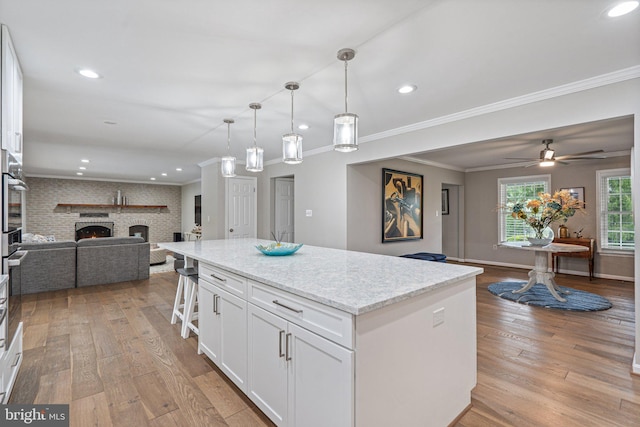 kitchen with open floor plan, light wood-style flooring, a center island, crown molding, and white cabinets