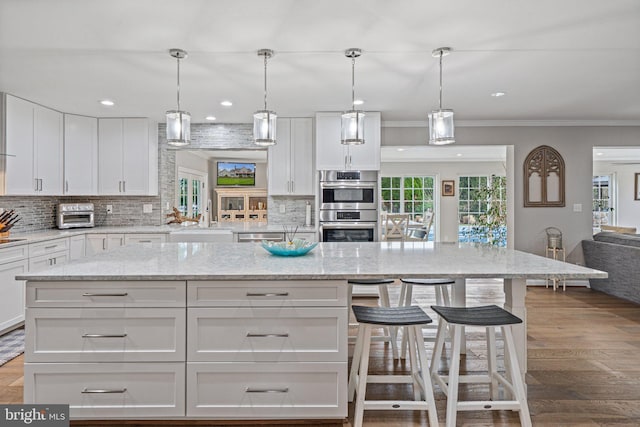 kitchen featuring a kitchen breakfast bar, white cabinetry, a center island, wood finished floors, and stainless steel appliances