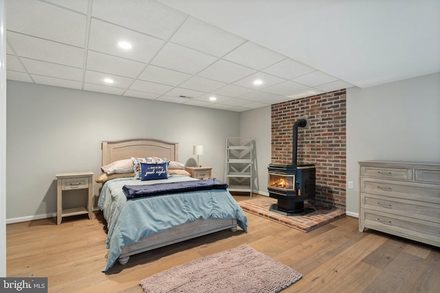 bedroom with a paneled ceiling, baseboards, recessed lighting, a wood stove, and wood finished floors