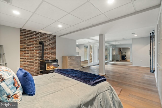 bedroom with recessed lighting, a wood stove, a drop ceiling, and wood finished floors