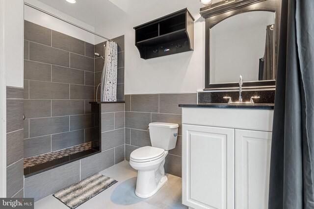full bathroom featuring toilet, tile walls, a tile shower, vanity, and a wainscoted wall