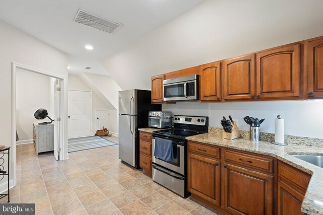 kitchen featuring brown cabinets, light stone counters, visible vents, and stainless steel appliances