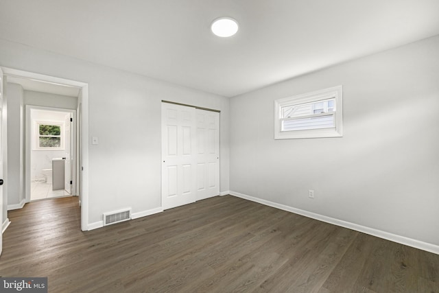 unfurnished bedroom featuring dark wood-type flooring, visible vents, multiple windows, and baseboards