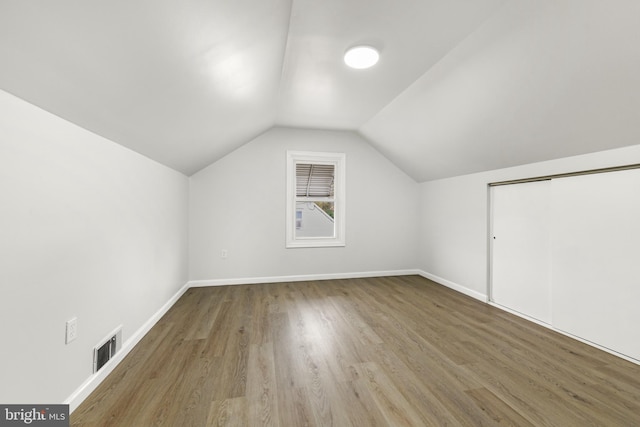 additional living space with wood finished floors, baseboards, lofted ceiling, and visible vents