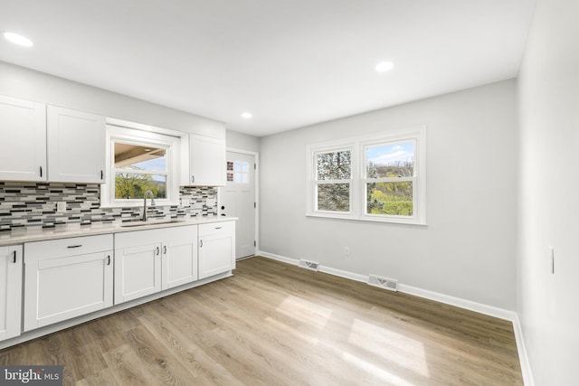 kitchen featuring baseboards, light countertops, backsplash, visible vents, and a sink
