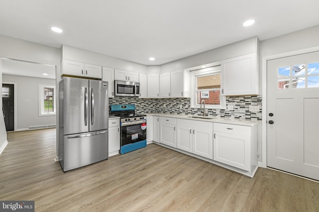 kitchen with tasteful backsplash, white cabinets, light countertops, a sink, and stainless steel appliances