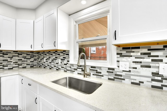 kitchen with a sink, tasteful backsplash, white cabinetry, and light stone countertops