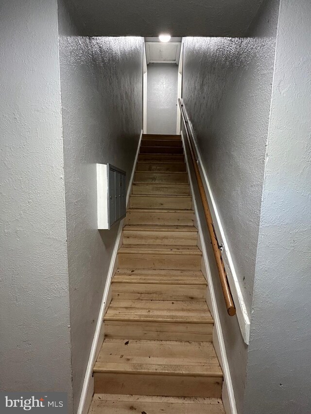 stairs featuring baseboards, attic access, a textured wall, and wood finished floors