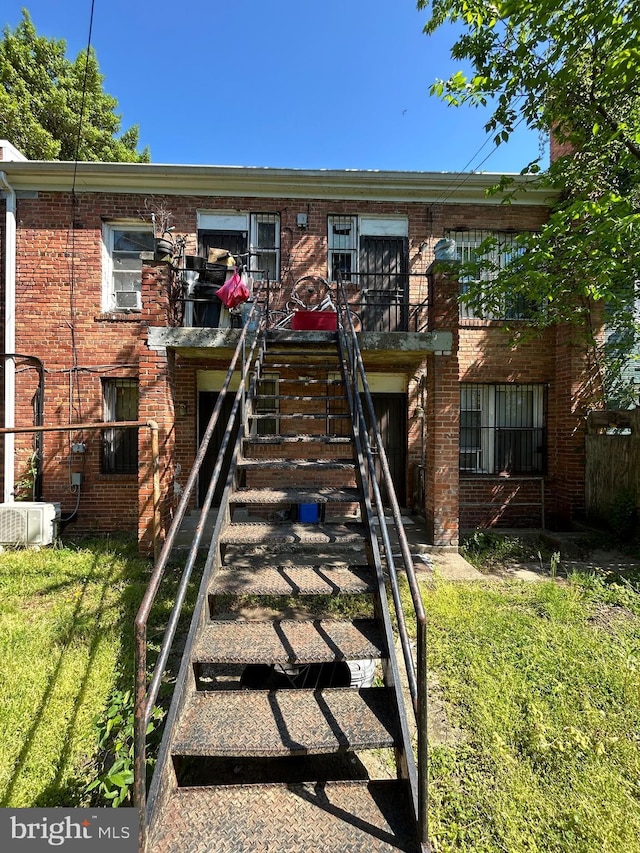 view of front facade with brick siding, a front yard, and stairway