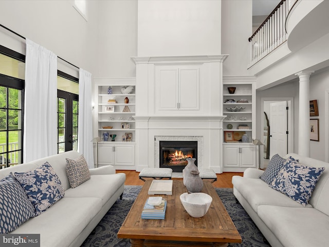 living room featuring wood finished floors, built in features, a fireplace, ornate columns, and a high ceiling