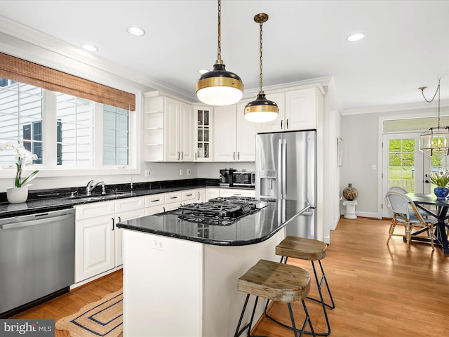 kitchen featuring hanging light fixtures, appliances with stainless steel finishes, a sink, white cabinetry, and crown molding