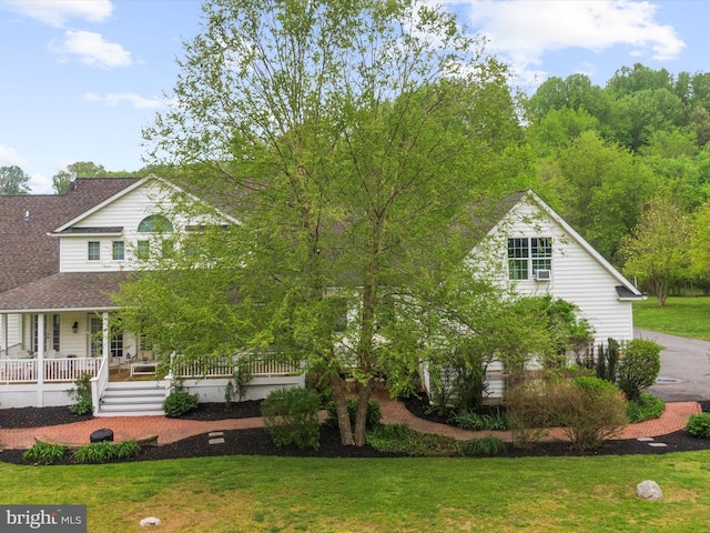 view of front of home with a porch, roof with shingles, and a front yard