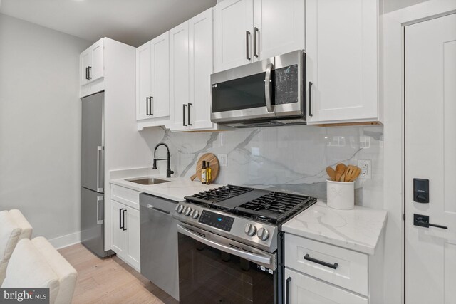 kitchen with light wood-style flooring, white cabinetry, light stone countertops, stainless steel appliances, and a sink
