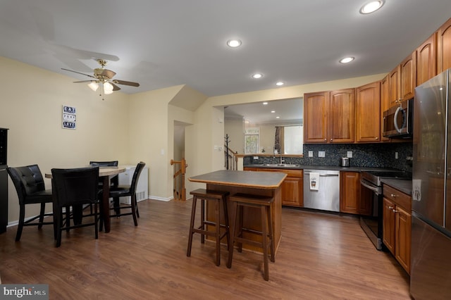 kitchen with a sink, dark countertops, backsplash, a breakfast bar, and appliances with stainless steel finishes
