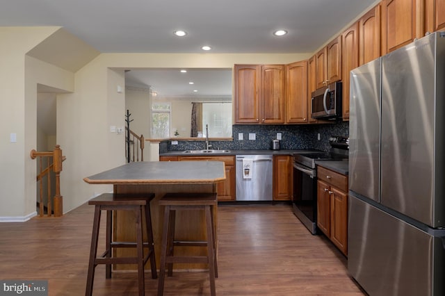 kitchen featuring stainless steel appliances, dark countertops, a sink, decorative backsplash, and dark wood-style flooring