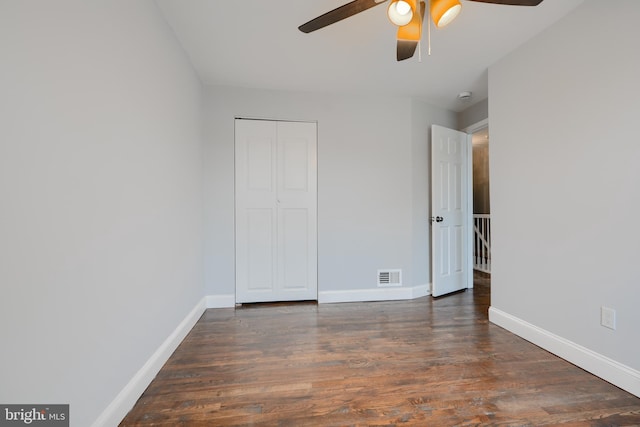unfurnished bedroom featuring dark wood-style flooring, visible vents, a closet, and baseboards