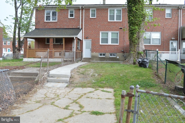 back of property with covered porch, brick siding, fence private yard, and a lawn