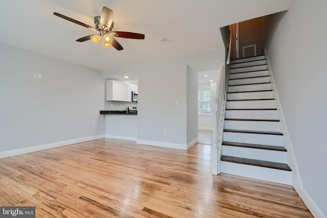 unfurnished living room featuring stairway, a ceiling fan, light wood-style flooring, and baseboards