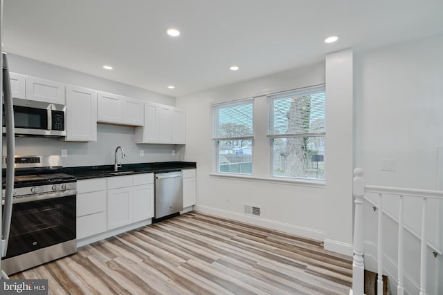 kitchen with a sink, light wood-type flooring, dark countertops, white cabinets, and appliances with stainless steel finishes