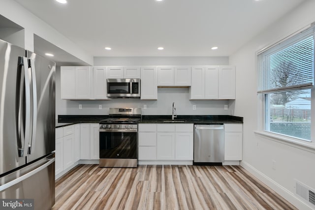 kitchen featuring a sink, light wood-type flooring, visible vents, white cabinetry, and appliances with stainless steel finishes