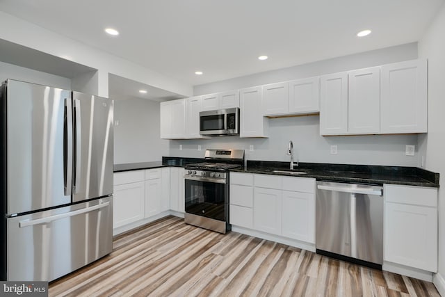kitchen with appliances with stainless steel finishes, white cabinetry, light wood-style flooring, and a sink