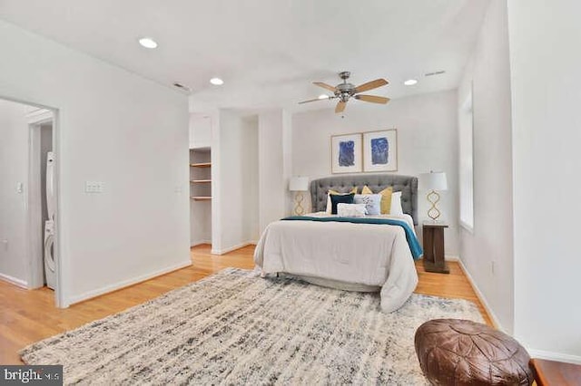 bedroom featuring baseboards, stacked washer and clothes dryer, a walk in closet, and wood finished floors
