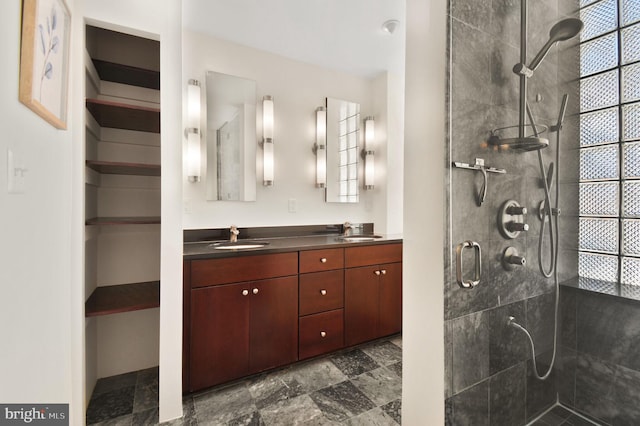 bathroom with a sink, a tile shower, and double vanity